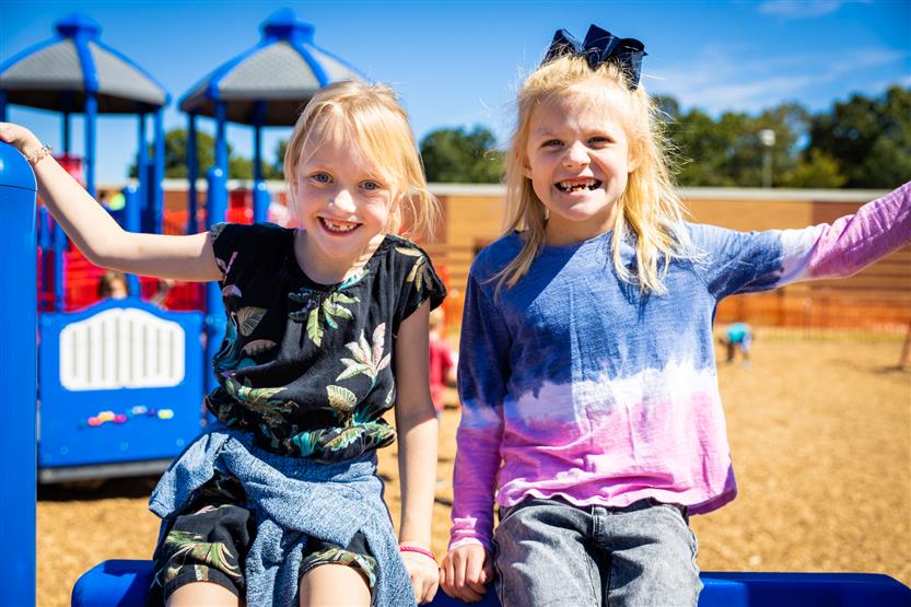 Two blonde girls smile on a playground